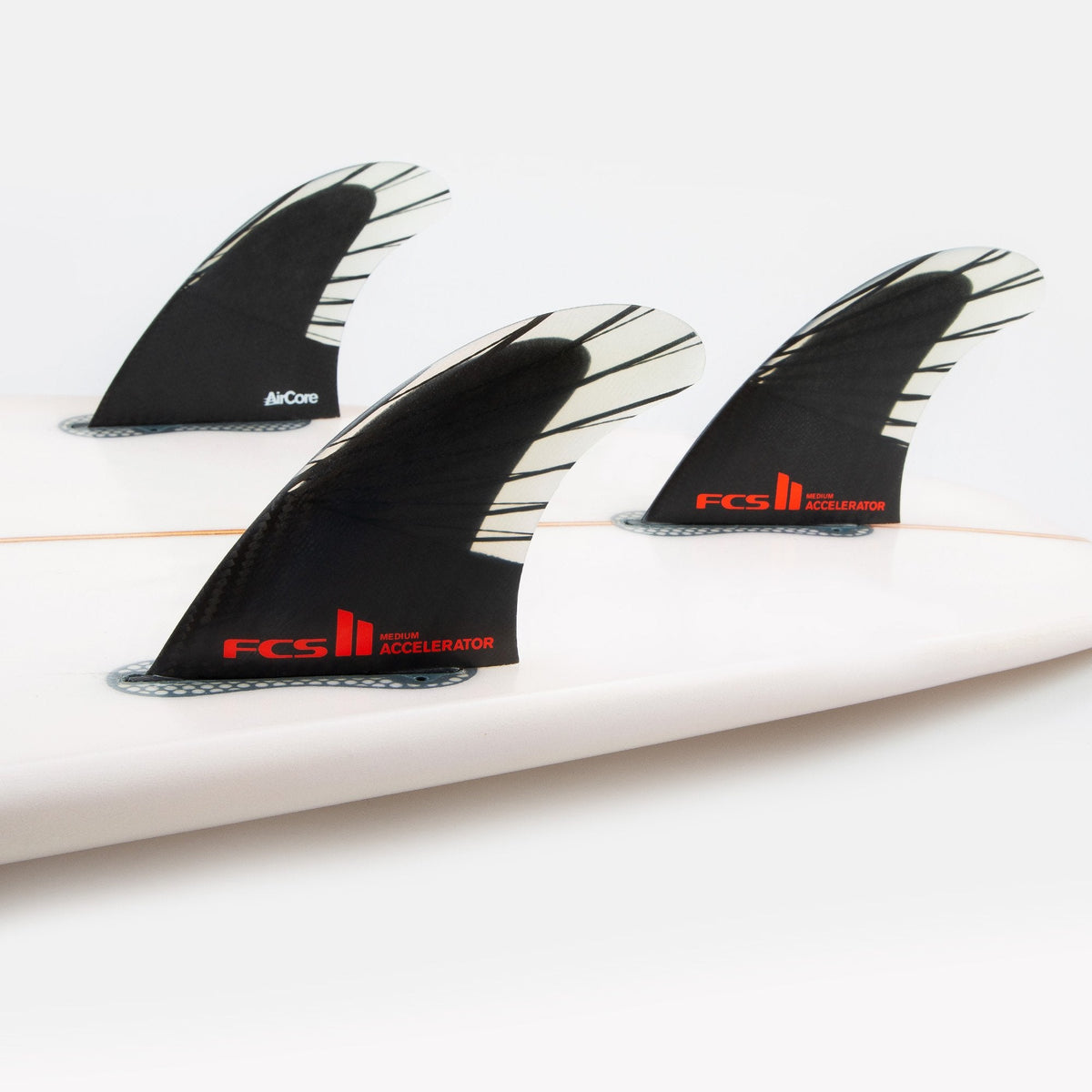 FCS II Accelerator Tri Fins - PC Carbon + AirCore: black and red carbon thruster fins installed on a surfboard