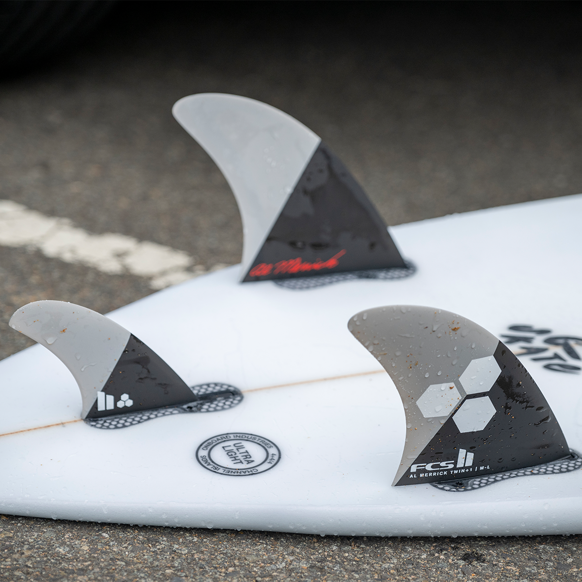 FCS II Al Merrick Twin + Stabiliser Fins - Performance Core: grey and Charcoal twin and stabiliser mounted on a board