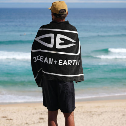 Ocean & Earth Priority Beach Towel: Black beach towel worn around the shoulders