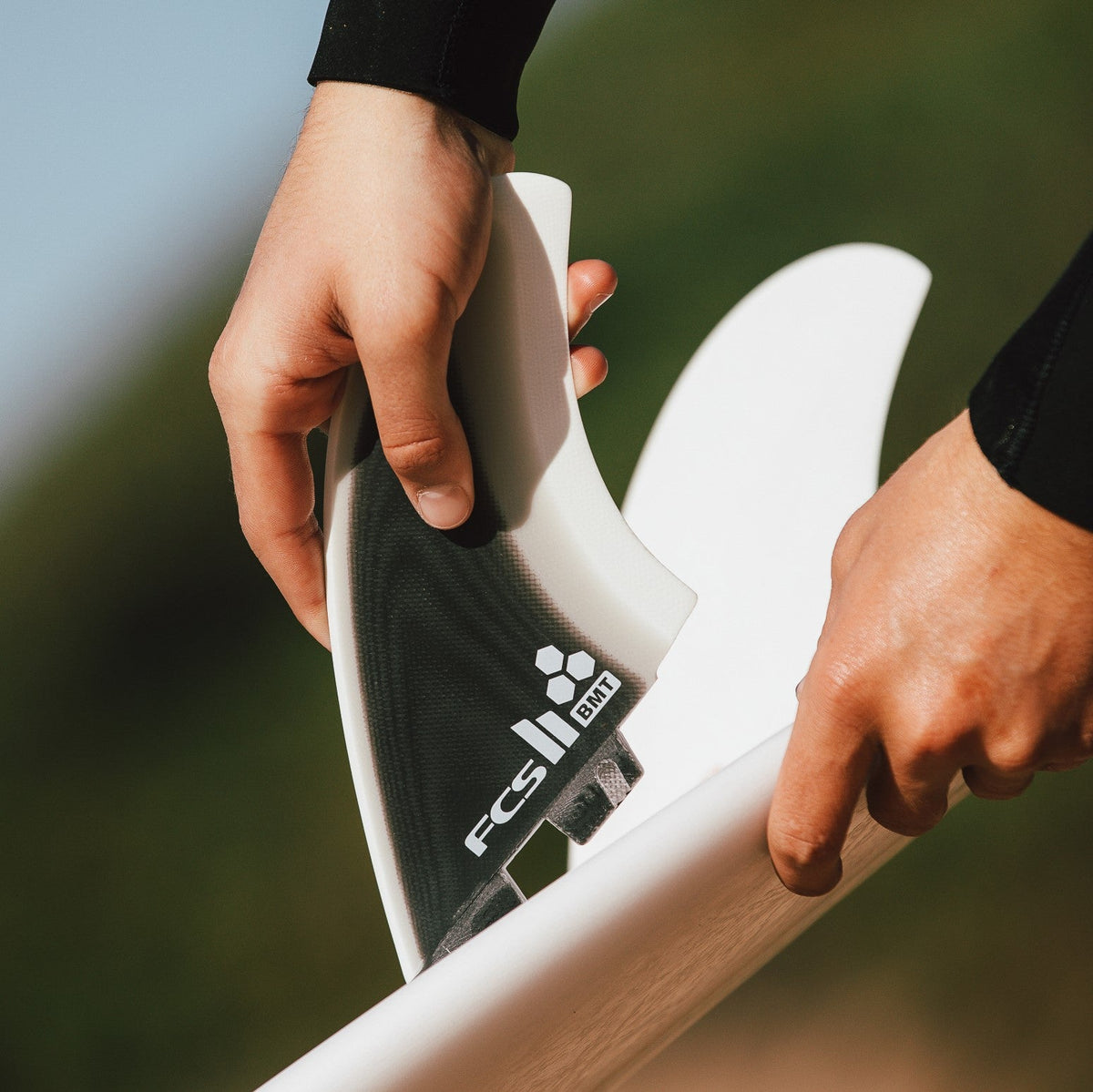 Hands fitting a Britt Merrick twin fin into a surfboard outdoors
