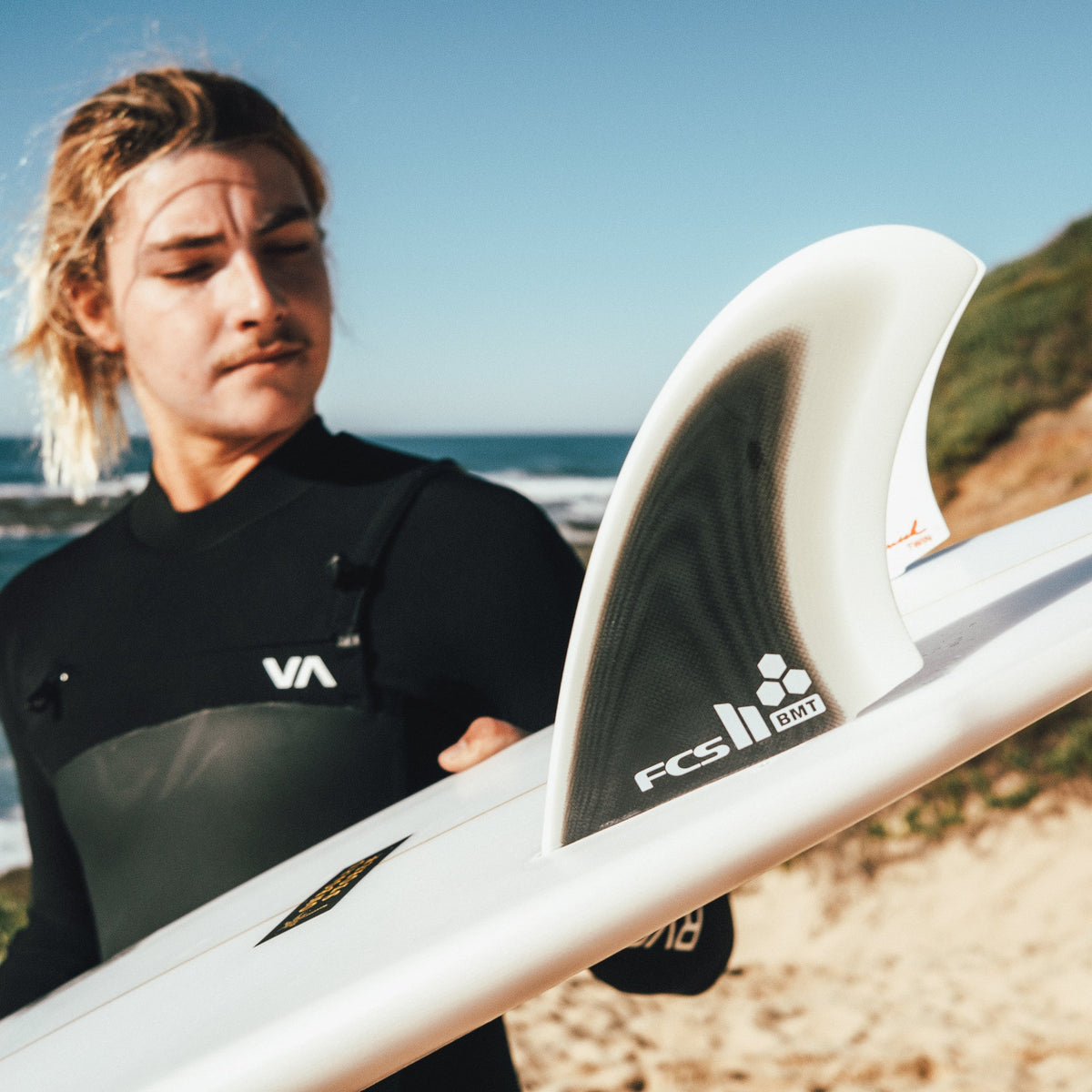 Surfer holding a board fitted with Britt Merrick twin fins by the beach