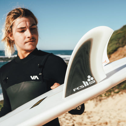 Surfer holding a board fitted with Britt Merrick twin fins by the beach