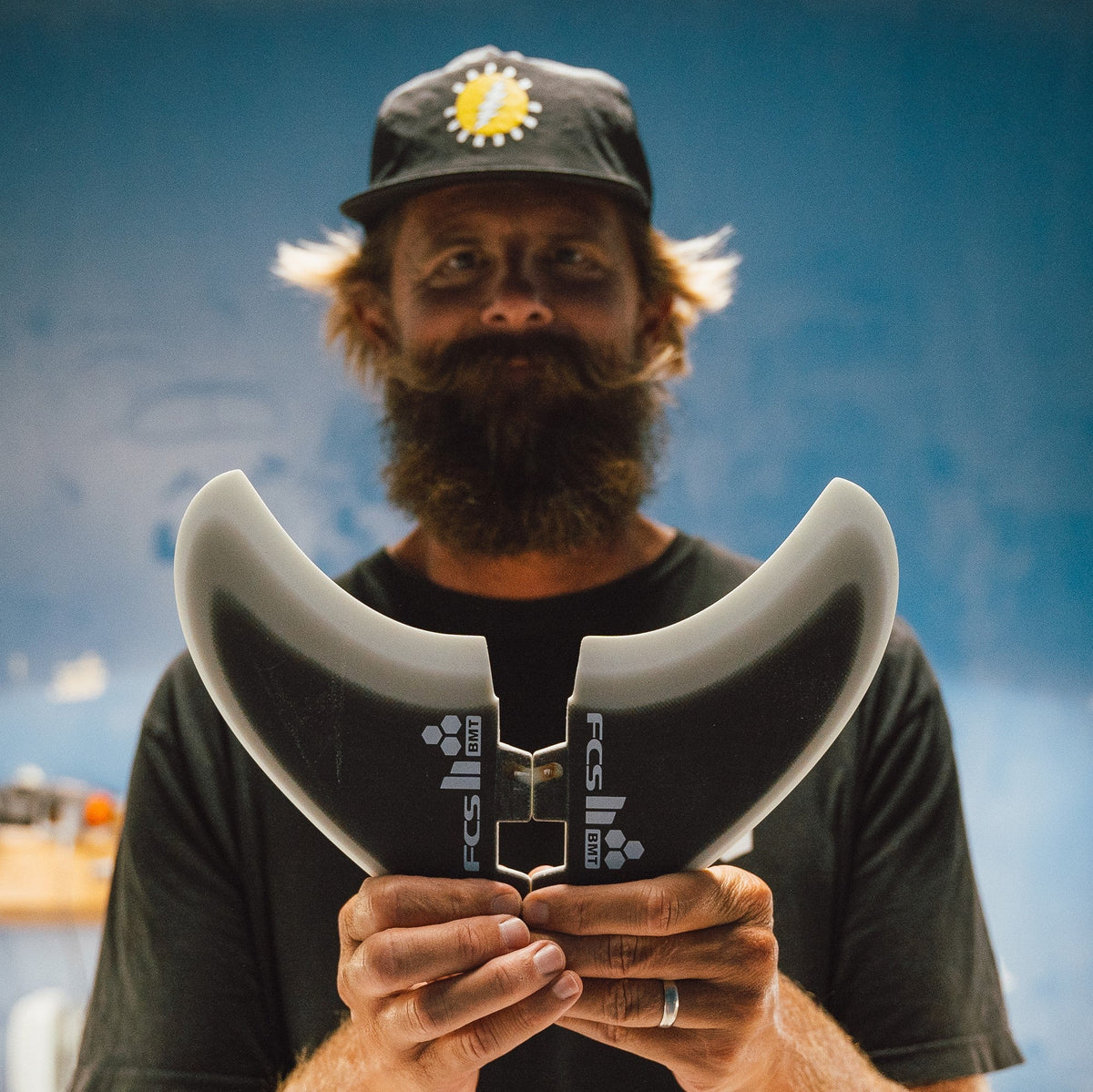 Britt Merrick holding a twin fin in front of his face outside a workshop