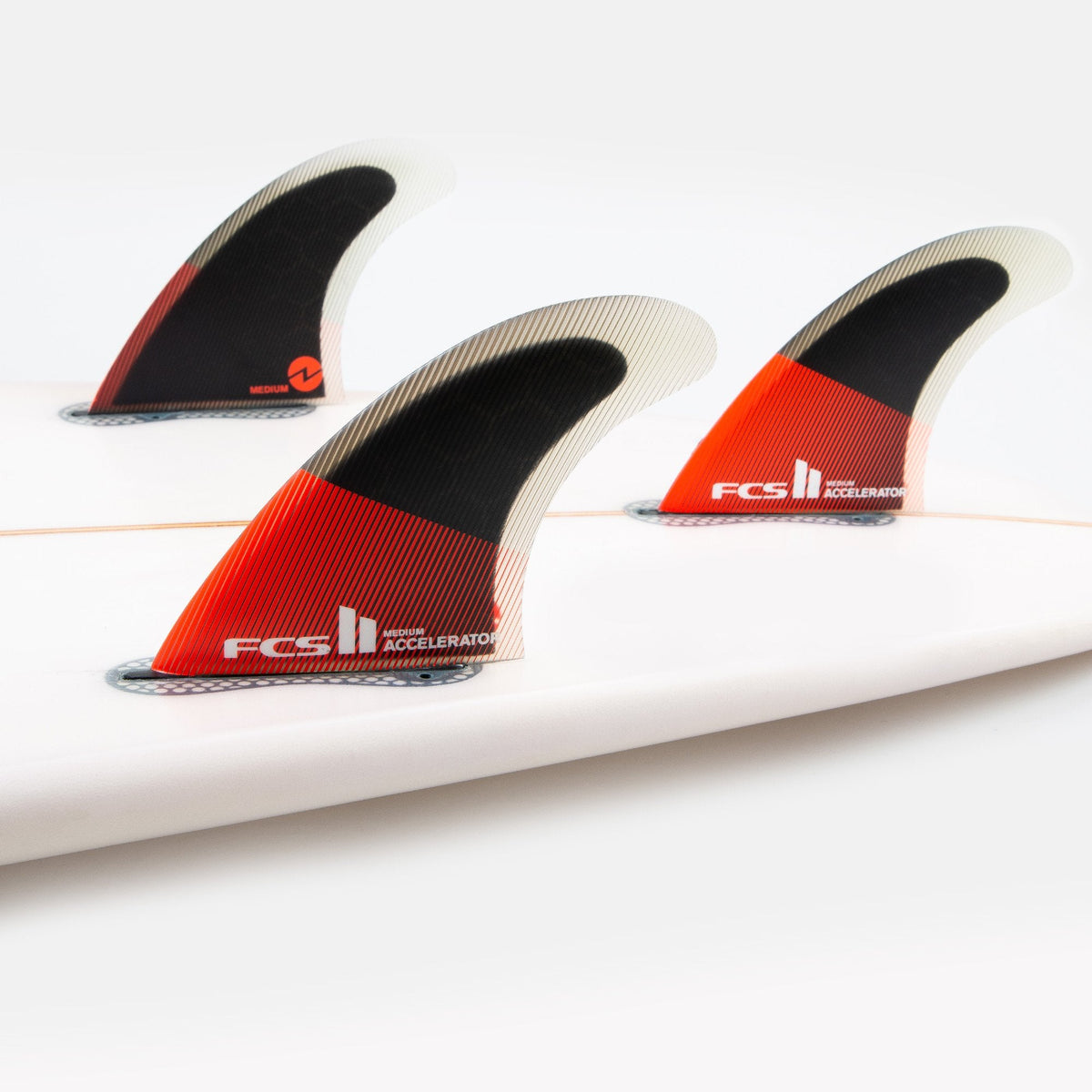 FCS II Accelerator Tri Fins - Performance Core: red and black thruster fins installed on a white board