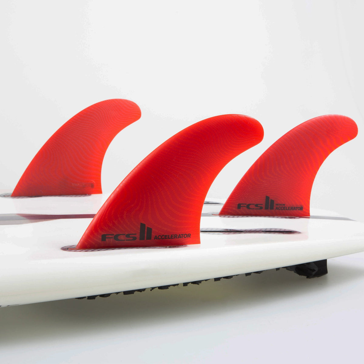 FCS II Accelerator Tri Fins - Eco Neo Glass: red thruster setup mounted on a white surfboard