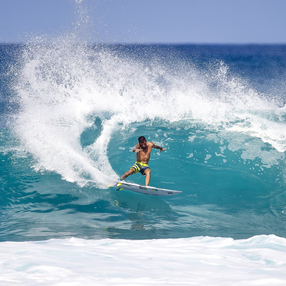 Filipe Toledo surfing beneath a turquoise barrel with spray behind him