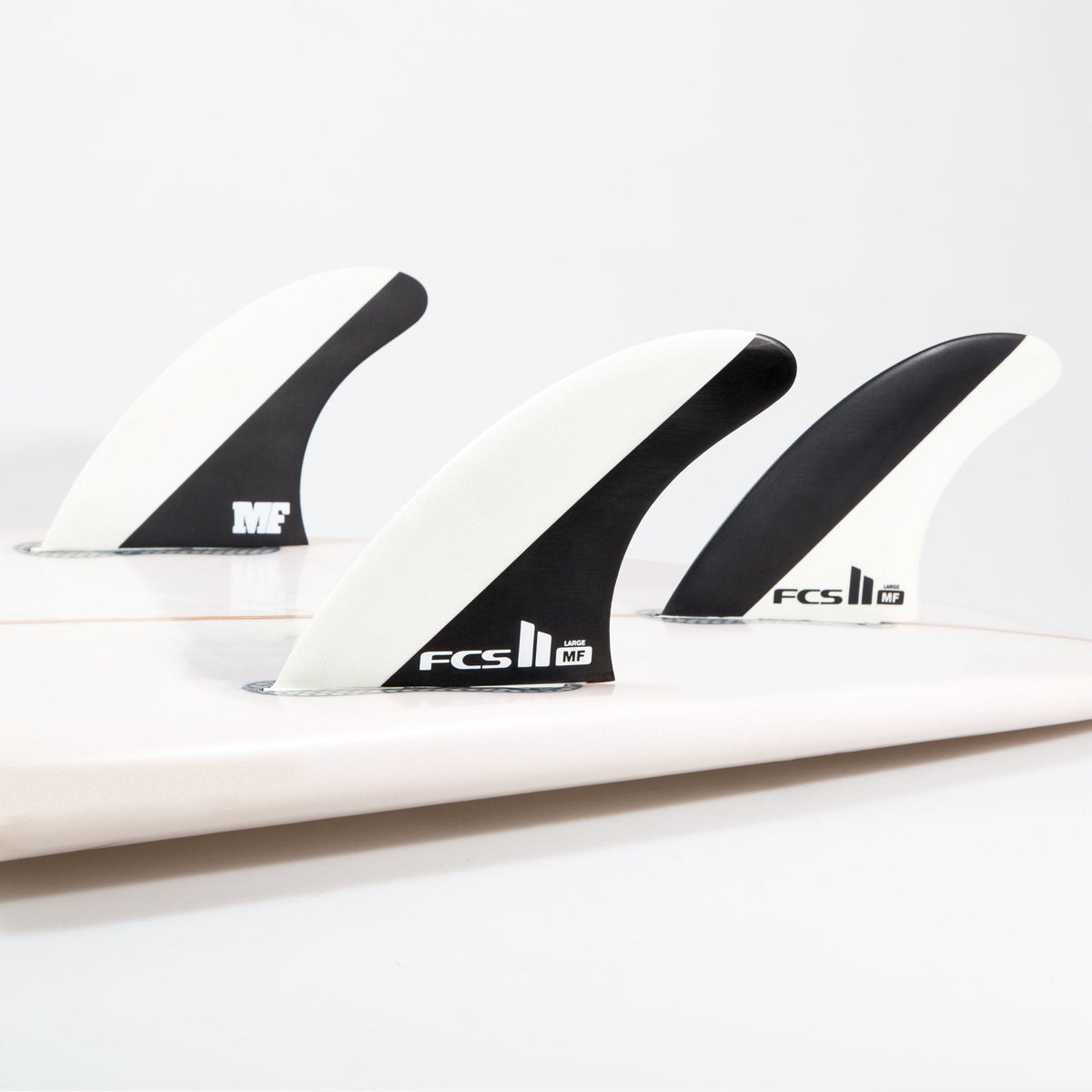 FCS II Mick Fanning Tri Fins - Performance Core: black and White thruster fins installed on a white board
