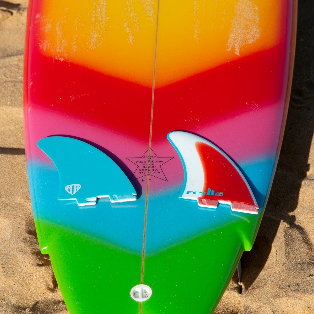 Blue and red Freeride twin fins on a brightly coloured surfboard standing outdoors