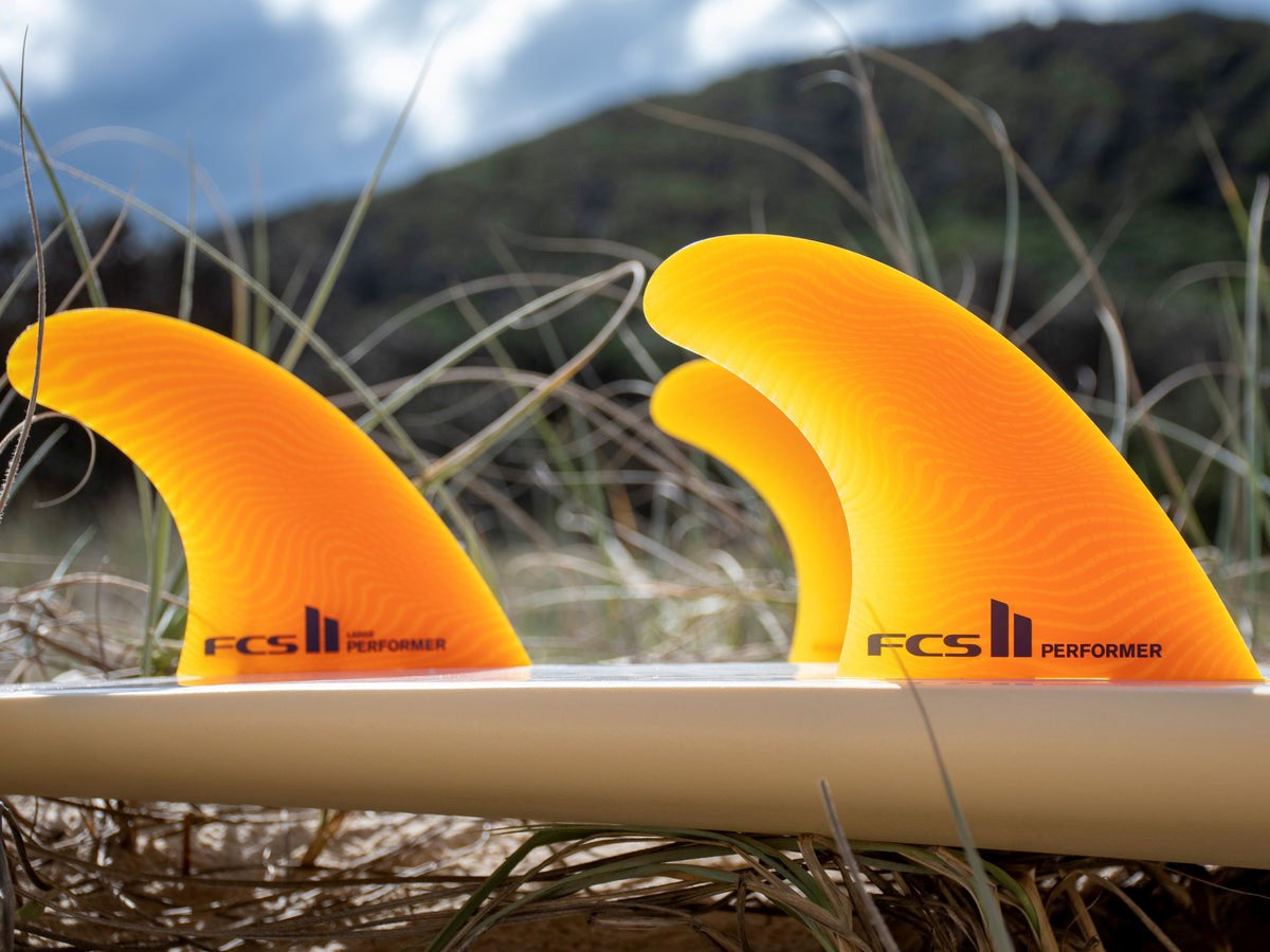 FCS II Performer Tri Fins - Eco Neo Glass: mango thruster fins installed on a white surfboard