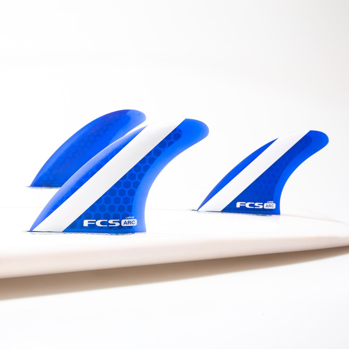 Blue Large FCS ARC thruster set mounted on a white surfboard