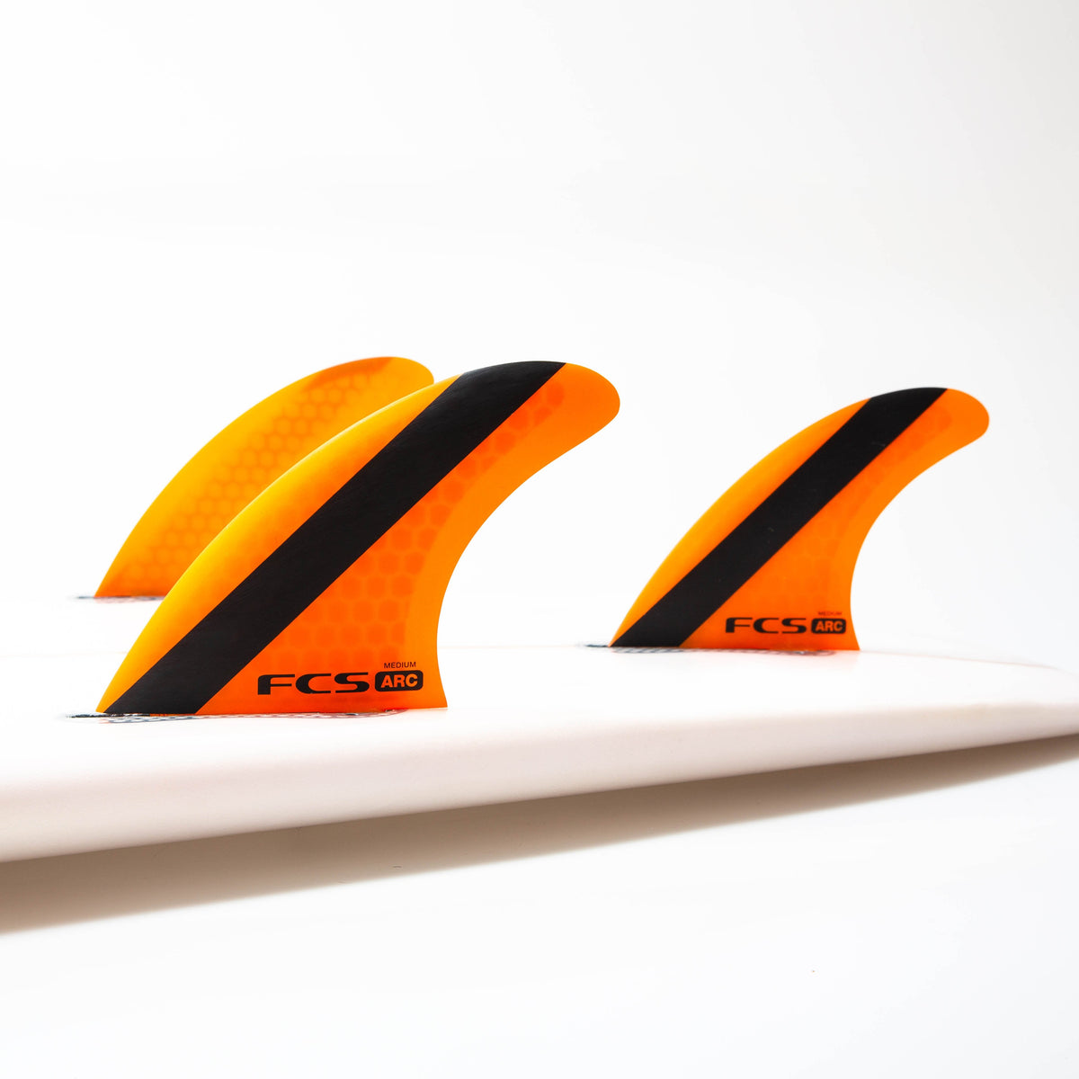 Orange Medium FCS ARC thruster set fitted to a white surfboard