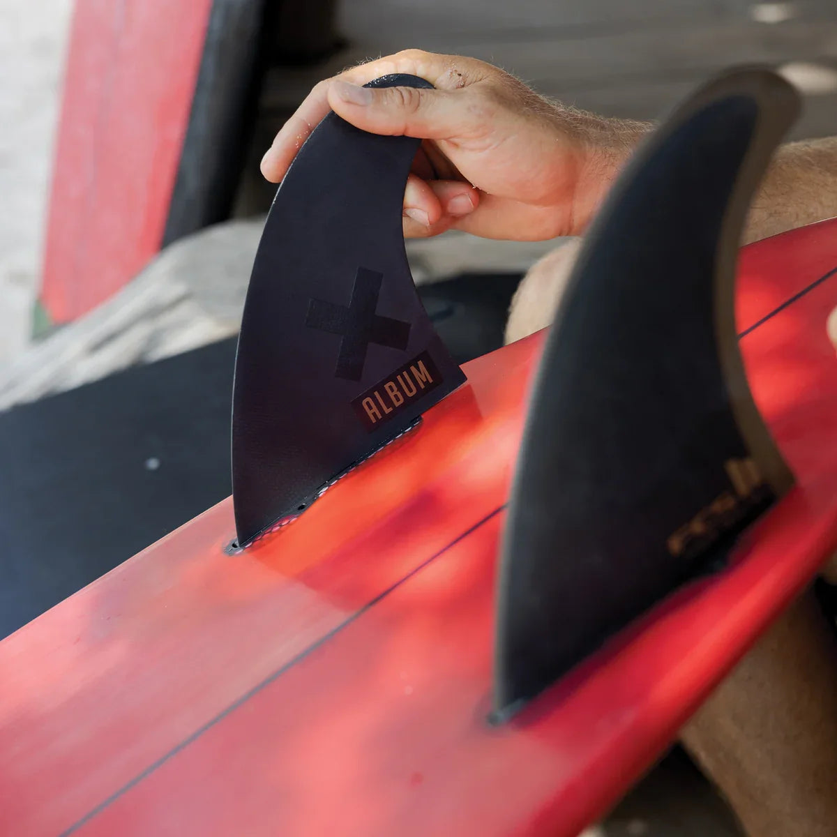 Hand installing an Album twin fin on a red and black surfboard