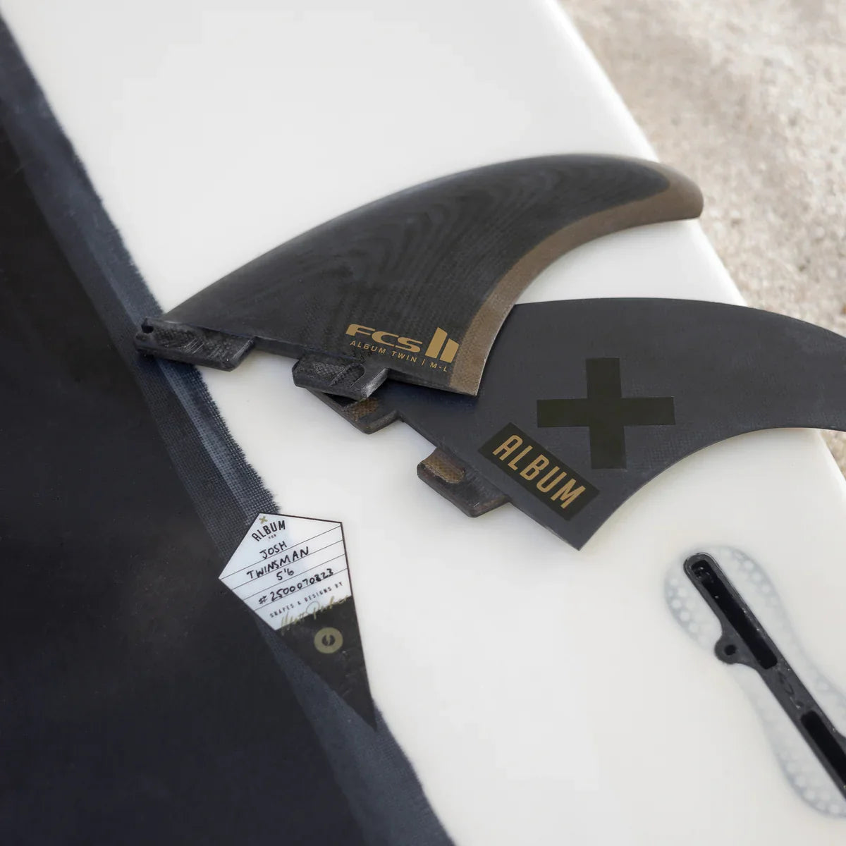 Album fin set, fin key and packaging arranged on a white surfboard