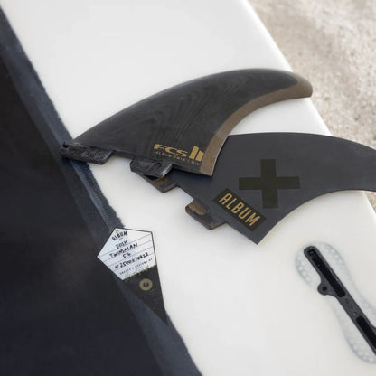 Album fin set, fin key and packaging arranged on a white surfboard