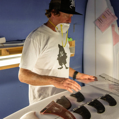 FCS II Christenson Keel - Performance Glass: shaper checking fins beside a workshop table