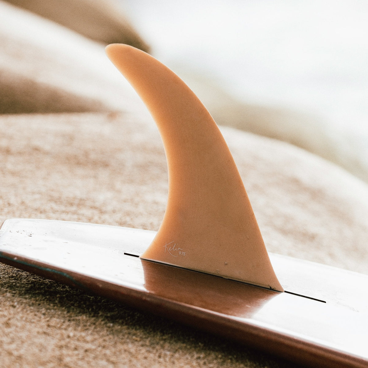 FCS II Kelia Moniz Longboard Fin - Performance Glass: peach coloured fin mounted on a longboard on the beach