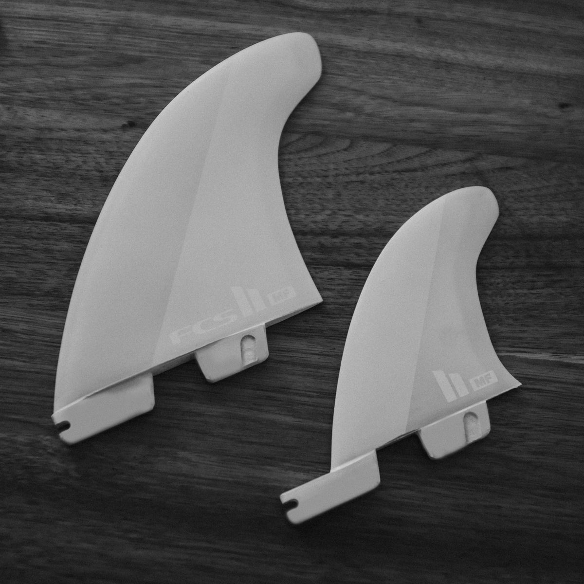 FCS II Mick Fanning Twin + Stabiliser Fins - PC + AirCore: two white fins lying on a dark wooden surface