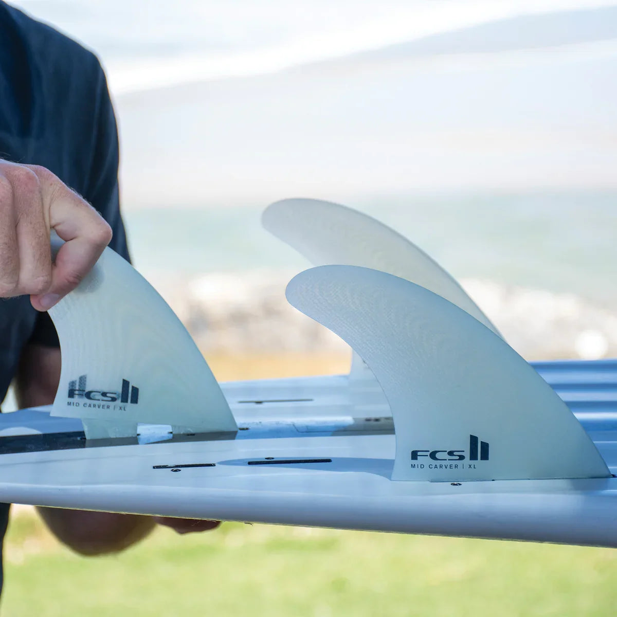 FCS II Mid Carver 2 + 1 Fin Set - Performance Glass: close view of the Clear fins being fitted to a board