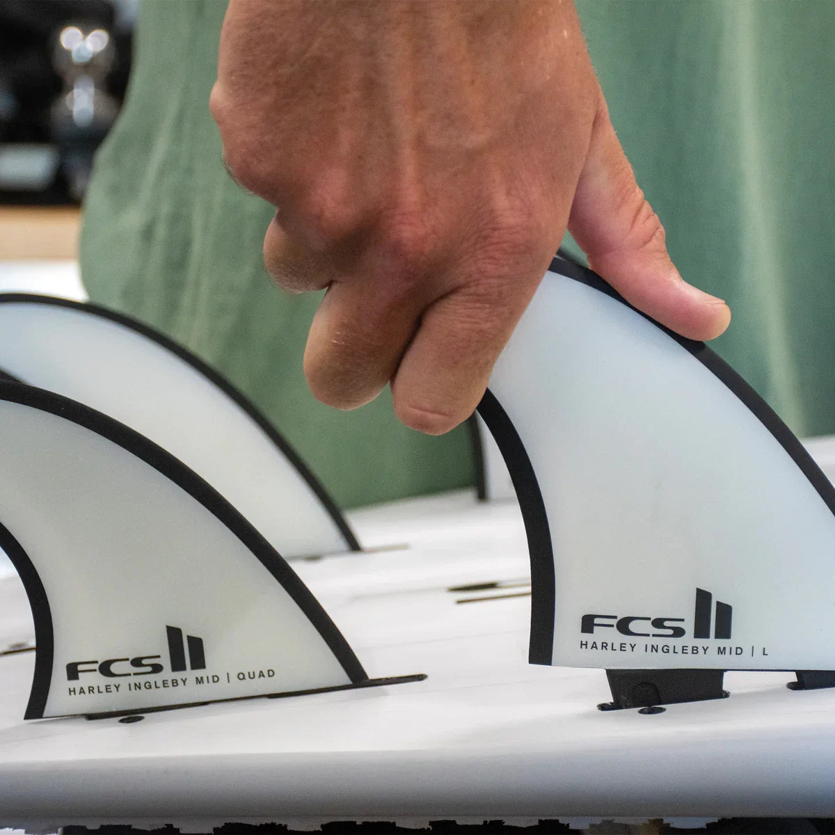 FCS II Harley Mid Tri-Quad Fin Set - Performance Core + AirCore: hand fitting a white outlined fin to a board