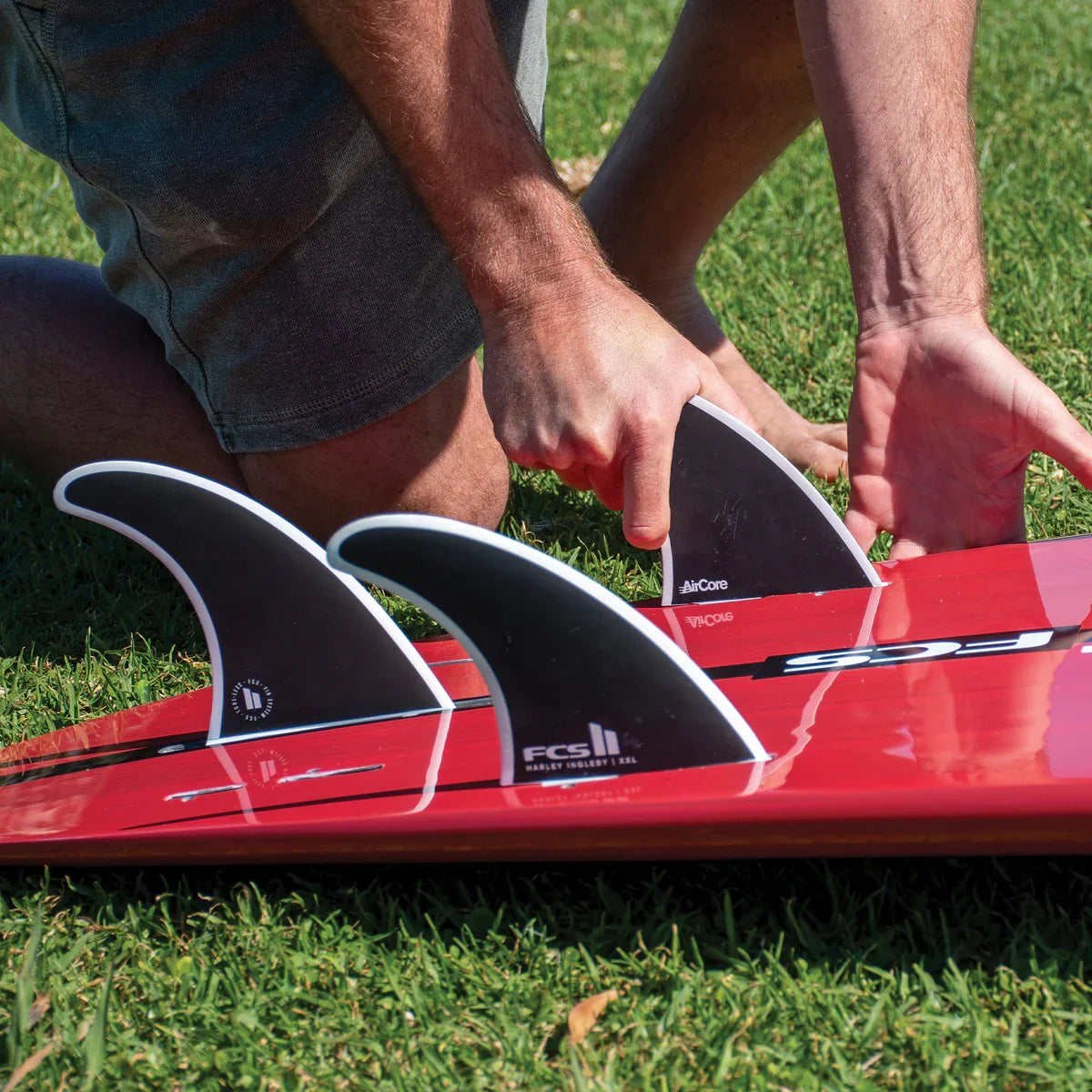 FCS II Harley Longboard Tri Fins - Performance Core: hands fitting the Harley tri setup to a red board