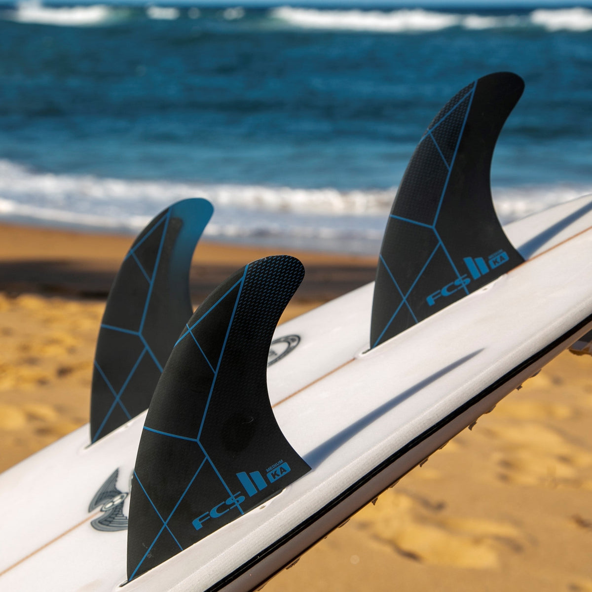 FCS II Kolohe Andino Tri Fins - Performance Core: black and Blue fins installed on a board beside the beach