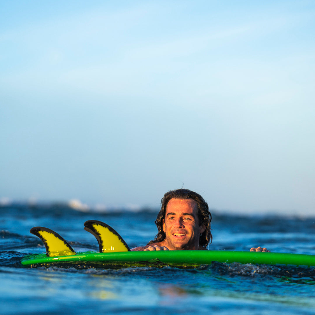 FCS II Mason Ho Tri Fins - PC + AirCore: mason Ho floating beside his green board with the fins visible