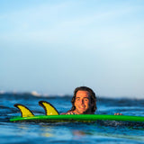 FCS II Mason Ho Tri Fins - PC + AirCore: mason Ho floating beside his green board with the fins visible