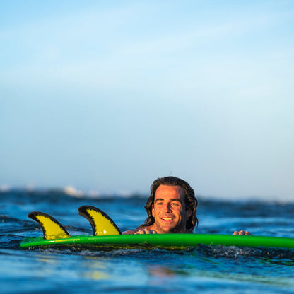 FCS II Mason Ho Tri Fins - PC + AirCore: mason Ho floating beside his green board with the fins visible