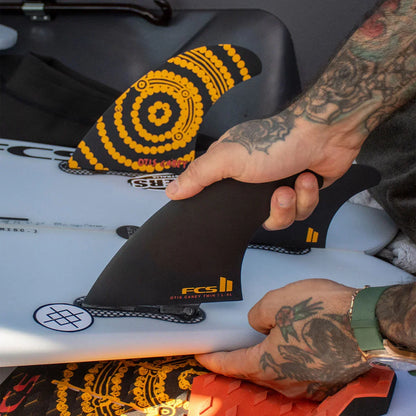 FCS II Otis Carey Twin + Stabiliser Fins - Performance Glass: hands showing the stabiliser beside the patterned twin fin