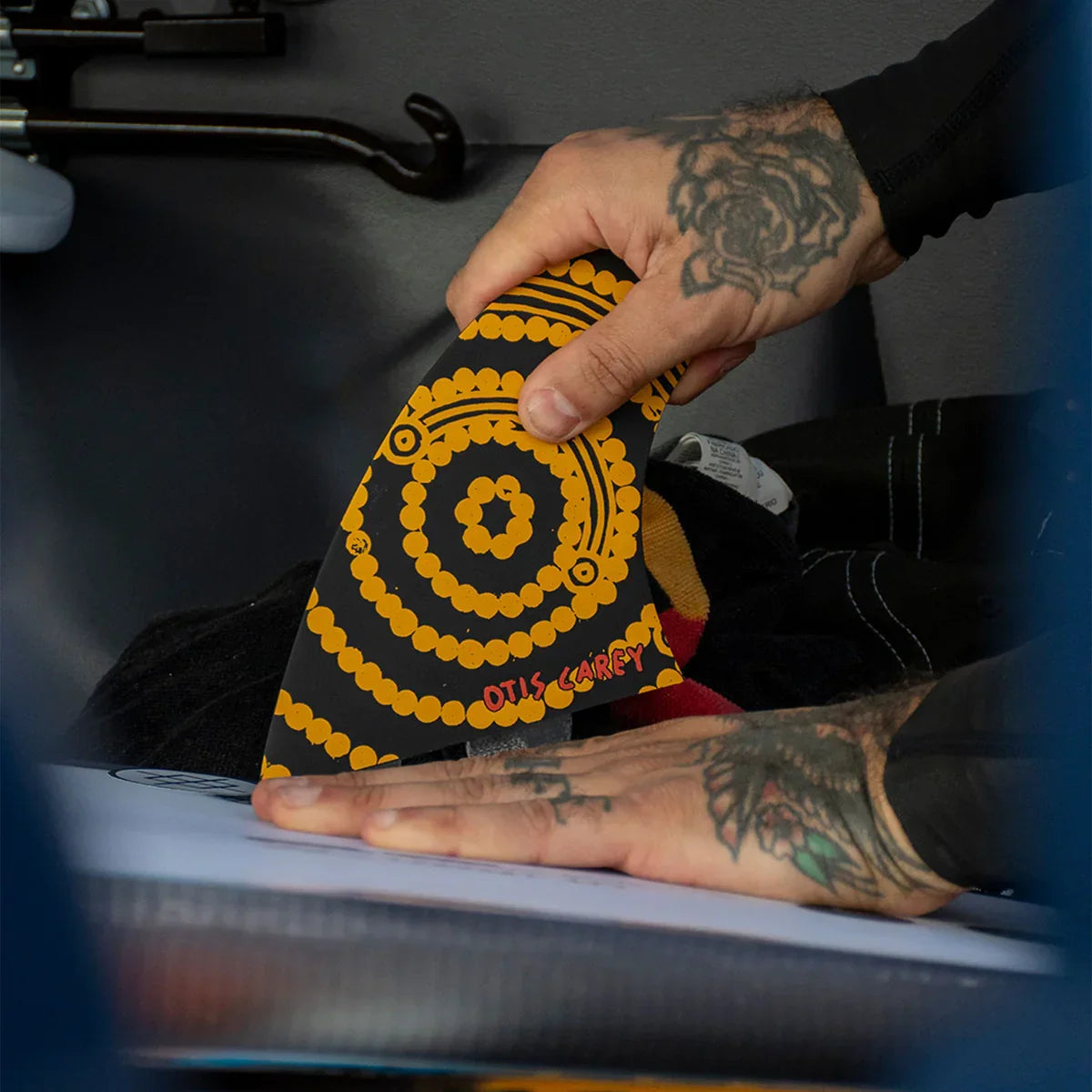 FCS II Otis Carey Twin + Stabiliser Fins - Performance Glass: tattooed hands holding the patterned Otis Carey fin