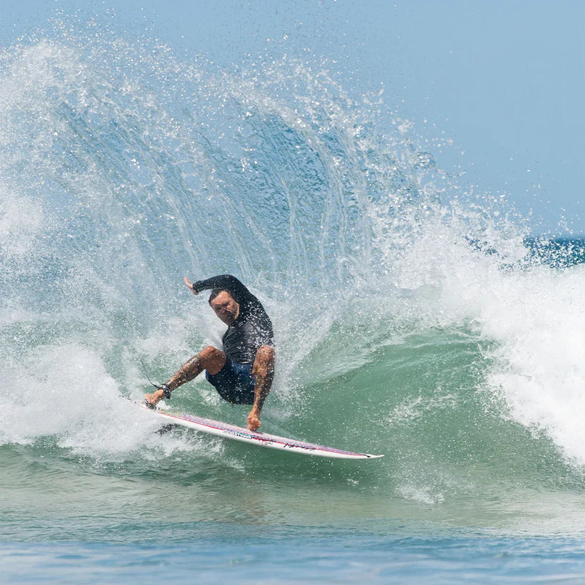 FCS II Otis Carey Twin + Stabiliser Fins - Performance Glass: surfer turning on a green wave with spray