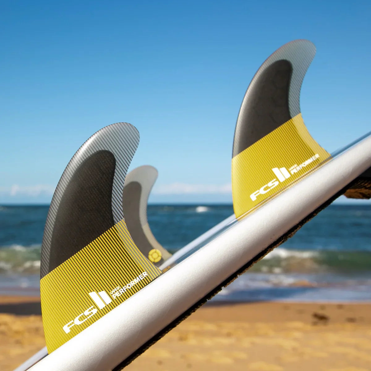 FCS II Performer Tri Fins - Performance Core: mango fins mounted on a surfboard at the beach