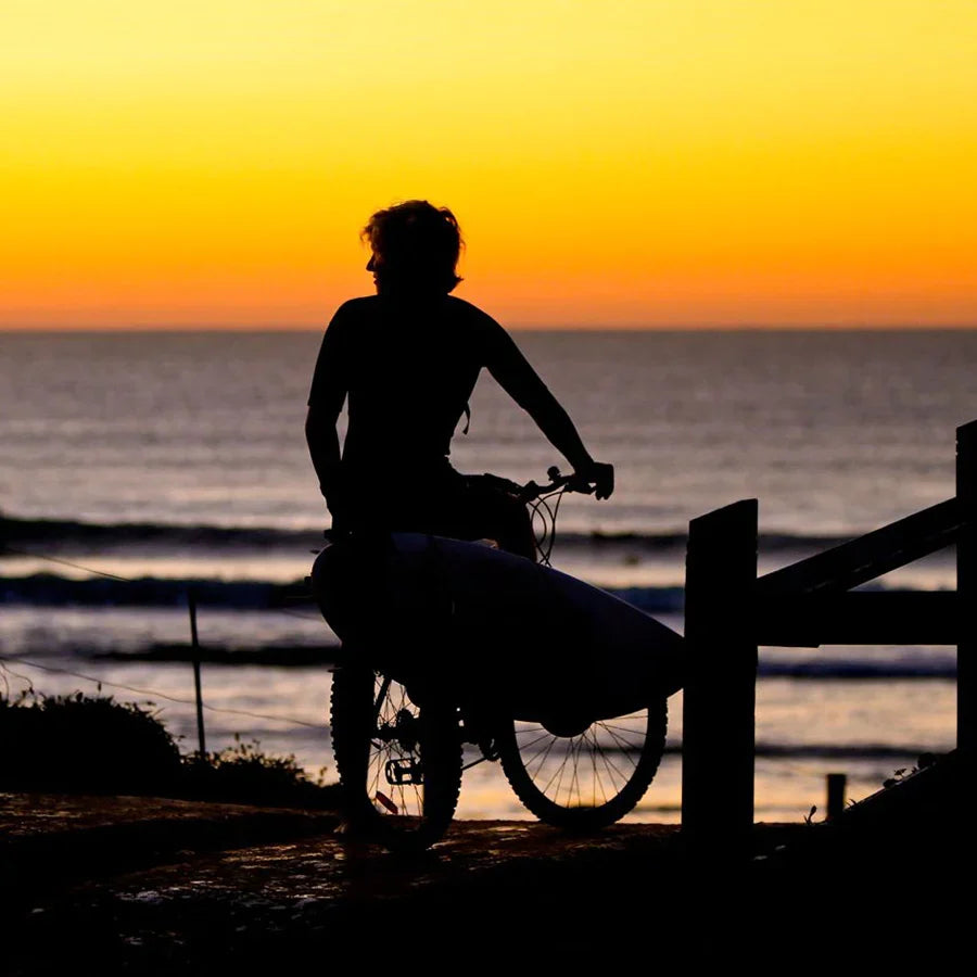 Ocean & Earth Side Loader Bike Rack: Cyclist carrying a surfboard at sunset