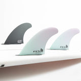 FCS II Sky Brown Tri Fins - Performance Core: seafoam and Lavender thruster fins installed on a white board