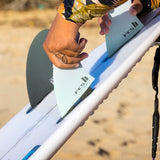 FCS II Sky Brown Tri Fins - Performance Core: close view of Sky fitting a fin to a white surfboard