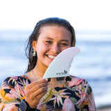 FCS II Sky Brown Tri Fins - Performance Core: sky Brown holding her signature fin beside the ocean